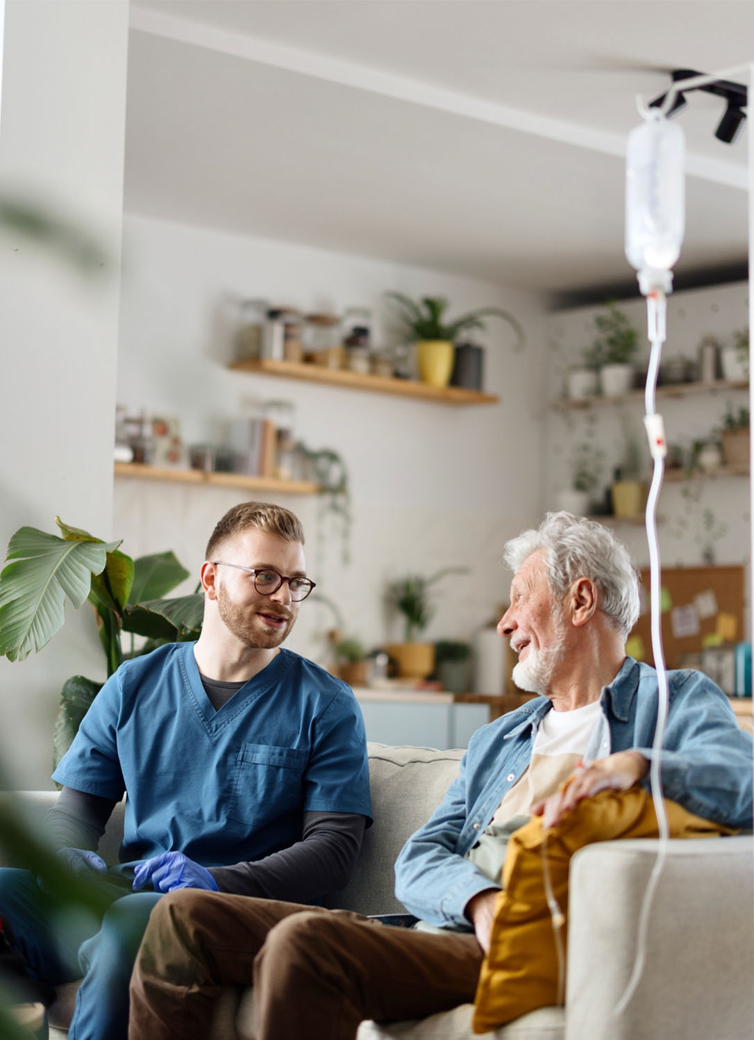 A registered nurse and patient sit on the couch smiling, sharing stories